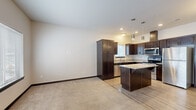 This two-story home in Rochester, MN offers a well-designed layout spread across two floors. The main level features an open-concept kitchen and living area, where rich dark-wood cabinetry, granite countertops, and a full suite of stainless steel appliances — including a refrigerator, range, microwave, and dishwasher — create a polished, functional space. A center island with pendant lighting serves as both a prep area and casual gathering spot, while a chandelier adds an elegant touch to the adjacent living area. Light wood-style flooring runs through the kitchen, transitioning to plush carpet in the living space. Upstairs, three well-proportioned bedrooms offer comfortable retreats, each with soft carpeting and ample natural light from windows. The primary bedroom includes a spacious walk-in closet with wire shelving. The two full bathrooms are finished with dark wood vanities, granite countertops, large mirrors, and distinctive hexagonal tile flooring. A dedicated laundry room with a full-size washer and dryer adds everyday convenience. Dark wood trim and door accents carry a cohesive, modern aesthetic throughout. A staircase with a dark wood railing connects the two levels, completing this thoughtfully appointed home.