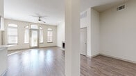 This single-floor residence offers a thoughtfully designed open layout with wood-look flooring extending throughout every room, creating a warm and cohesive aesthetic. The main living area is a generously proportioned space anchored by a classic fireplace with a clean white surround. Arched windows and a glass-panel entry door flood the room with natural light, while a ceiling fan adds functional comfort. The elevated ceilings contribute to an open, airy atmosphere.

An adjoining area serves as a flexible dining or flex space, bathed in sunlight through large windows with views of the surrounding area. A dedicated built-in desk nook features rich dark wood cabinetry above a floating white countertop, providing an ideal workspace or study area.

The bathroom is well-appointed with a dark wood vanity, white countertop, a glass-enclosed walk-in shower, a soaking tub, and brushed nickel fixtures throughout. A spacious walk-in closet with wire shelving systems offers ample storage. The in-unit laundry area accommodates a full-sized washer and dryer side by side, adding everyday convenience. Throughout the residence, a neutral color palette of warm whites and beige tones creates a clean, inviting ambiance ready for personalization.