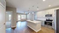 This two-bedroom, two-bathroom unit at 3125 Furr Ct in Charlotte, NC offers a well-designed single-level layout with a comfortable, modern aesthetic throughout. The open living area features warm wood-style flooring, neutral beige tones, and a ceiling fan, with a glass door and large windows that invite abundant natural light and outdoor views. The space flows seamlessly into the kitchen, which is appointed with white shaker cabinetry, gray lower cabinets, white quartz countertops, a subway tile backsplash, stainless steel appliances including a French door refrigerator and electric range, recessed lighting, and a pendant-lit island that adds both workspace and visual appeal. The living room continues the wood-style flooring and provides ample room for flexible furniture arrangements. Both bedrooms are carpeted and include ceiling fans and large windows with outdoor views. The primary bedroom connects to a private en-suite bathroom featuring a dual-sink vanity with gray cabinetry and wood-style flooring. The second bathroom offers a tub-shower combination and a single-sink vanity. Each bedroom is complemented by a dedicated walk-in closet with wire shelving systems, providing generous storage throughout the unit.