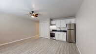 Located at 2497 N Park Ave in Tucson, Arizona, this efficiently designed single-floor unit offers a clean, modern aesthetic within a cozy footprint. The open-concept main area seamlessly integrates the living space and kitchen, creating a functional and versatile layout. Light wood-look tile flooring runs throughout, lending a bright, cohesive feel to the interior. A ceiling fan with an integrated light fixture provides both air circulation and ambient lighting, complementing the wall-mounted A/C unit for year-round comfort. Natural light enters through a window fitted with blinds, enhancing the airy atmosphere of the main room.

The kitchen is thoughtfully appointed with crisp white cabinetry, dark countertops, a stainless steel refrigerator, a stainless steel range with oven, and an under-cabinet range hood. A double-door closet adjacent to the kitchen provides convenient storage. The bathroom features wood-look tile flooring consistent with the rest of the unit, a white vanity with a dark countertop, a mirrored medicine cabinet, and a fully tiled walk-in shower with classic white subway tiles, a decorative mosaic accent border, and hexagonal floor tiles. The overall design is clean and contemporary, making this Tucson unit an efficient and well-finished space.