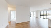 This thoughtfully designed single-floor residence offers three bedrooms, three bathrooms, and a generous overall footprint that balances open communal areas with private living spaces. The open-concept kitchen and living room serve as the heart of the home, bathed in natural light from large, black-framed floor-to-ceiling windows that frame outdoor views. The kitchen features rich dark wood cabinetry, light lower cabinets, white quartz countertops, a white subway tile backsplash, stainless steel appliances including a range with hood, and light wood-style flooring that extends throughout the main living areas. The expansive living room benefits from a bright, airy feel with crisp white walls and multiple large windows. Each of the three bedrooms offers a calm, neutral palette with plush carpeting and its own closet, complete with built-in hanging rods. The three bathrooms are clean and modern, featuring white tile, soaking tub and shower combinations with chrome fixtures, and vanities with wood-tone cabinetry. A dedicated in-unit laundry room houses a stacked washer and dryer. A hallway connects the spaces efficiently, and three closets provide ample storage throughout this well-appointed residence.
