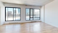 Located at 375 Rue de la Concorde in the heart of Montréal, this modern 2-bedroom, 1-bathroom unit delivers a compelling blend of contemporary design and urban living. Exposed concrete ceilings throughout lend an industrial character, while light-toned hardwood flooring creates a warm, cohesive aesthetic across the living spaces.

The open living area is a standout, anchored by expansive floor-to-ceiling windows with black frames that flood the space with natural light and offer panoramic views of the Montréal skyline. A sliding glass door provides access to an outdoor terrace, further extending the connection to the city.

The kitchen is efficiently designed with two-tone cabinetry — white upper cabinets paired with wood-finish lower units — complemented by a white subway tile backsplash, dark countertops, and a full suite of stainless steel appliances including a refrigerator, range, dishwasher, and over-the-range microwave.

Both bedrooms feature the same large-format windows with impressive city views, exposed concrete ceilings, and hardwood floors. The primary bedroom includes a built-in closet with bi-fold doors.

The bathroom is finished with large-format stone-look porcelain tile on both the floors and walls, a soaking tub, and a sleek floating vanity with a rectangular undermount sink and mirrored medicine cabinet.