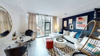 This single-floor residence is thoughtfully designed with a contemporary aesthetic and a well-organized layout. The living area serves as the centerpiece of the space, featuring floor-to-ceiling sliding glass doors that flood the room with natural light and open to an outdoor balcony. A bold navy accent wall adds depth and contrast against the light wood flooring that runs throughout the unit. The open-plan arrangement comfortably accommodates both a seating area and a dining nook.

The kitchen is outfitted with stainless steel appliances, including a range, built-in microwave, and refrigerator. Two-tone cabinetry pairs warm wood lower cabinets with crisp white upper cabinets, complemented by a marble-style backsplash and clean quartz countertops. Recessed lighting and under-cabinet lighting ensure excellent visibility.

A well-lit hallway, accented with recessed lighting and a stylish barn door, connects the main living area to the private spaces. The bedroom offers a calm retreat with a walk-in closet providing organized shelving. The bathroom features classic white subway tile surrounding a full soaking tub and shower combination, with clean chrome fixtures completing the look.
