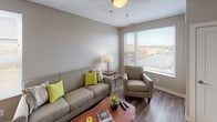 This single-floor residence offers a thoughtfully designed layout with a clean, modern aesthetic. The open-concept living and kitchen area serves as the heart of the unit, where warm hardwood-style flooring flows seamlessly throughout. The living room is bright and inviting, featuring large windows that allow abundant natural light and offer views of the surrounding neighborhood. A dedicated seating area provides a comfortable and functional space for relaxing or entertaining.

The kitchen is well-equipped and efficient, showcasing white shaker-style cabinetry, granite-look countertops, a classic subway tile backsplash, and a full suite of stainless steel appliances including a refrigerator, range, and built-in microwave. A breakfast bar with seating connects the kitchen to the living space, enhancing the open, social atmosphere.

The unit includes two bedrooms, each finished with plush carpeting and windows that bring in natural light. One bedroom features a walk-in closet accessible through sliding doors, offering generous storage. The full bathroom is clean and functional, featuring a white vanity, tile flooring, and a shower-tub combination with a marble-patterned curtain. Neutral tones and consistent finishes throughout the unit create a cohesive and welcoming ambiance.