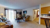 This single-floor 2-bedroom, 1-bathroom residence offers a thoughtfully designed layout that balances comfort and functionality. The living room serves as the heart of the home, featuring plush wall-to-wall carpeting, a textured ceiling, and a large sliding glass door that floods the space with natural light while providing access to the outdoors. A wall-mounted flat-screen TV and ample seating space make this an ideal area for relaxing or entertaining.

Adjacent to the living area, the dining space accommodates a round glass-top table with seating for four, positioned near the entry door for a welcoming feel. The kitchen is clean and efficient, offering white cabinetry with wood-tone accents, light flooring, and full-size appliances including a refrigerator.

Both bedrooms are generously sized with soft carpeting, ceiling fans with light fixtures, and windows that allow natural light to filter in. Each room comfortably fits a full-size bed along with additional furniture. The full bathroom features a vanity with ample counter space and light-toned flooring, providing a clean and practical environment.

Throughout the residence, neutral tones and consistent finishes create a cohesive, inviting ambiance well-suited for everyday living.