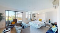 This single-floor studio is designed to maximize function and comfort within an open-plan layout. The main living area seamlessly integrates sleeping, lounging, and dining zones, centered around a built-in Murphy bed with integrated shelving and a dedicated workspace — an efficient solution that keeps the space feeling airy and versatile. Light hardwood flooring flows throughout, complementing the crisp white walls and clean-lined aesthetic.

Large sliding glass doors and floor-to-ceiling windows flood the interior with abundant natural light and provide direct access to a private outdoor balcony, which offers open views of the surrounding cityscape. The living area accommodates a comfortable seating arrangement alongside a media wall with open shelving, ideal for display and storage.

The kitchen is thoughtfully equipped with stainless steel appliances including a refrigerator, electric range, microwave, and dishwasher, all paired with granite countertops, dark lower cabinetry, and white upper cabinets for a modern two-tone contrast.

The bathroom features a full tub-shower combination, a floating vanity with a granite countertop, and a wide mirror, finished with the same light hardwood flooring found throughout. A wall-mounted mini-split system provides climate control throughout the unit.