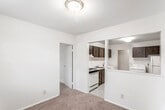 This single-floor residence offers a practical and well-organized layout across several distinct living spaces. The spacious living room is anchored by sliding glass doors fitted with vertical blinds, providing access to a balcony and allowing natural light to flow throughout. Neutral-toned carpeting extends across the living areas and bedrooms, contributing to a cohesive, understated aesthetic.

The kitchen is outfitted with dark wood cabinetry, a gas range, dishwasher, and a single-basin sink. A pass-through opening connects the kitchen to the adjacent living and dining areas, enhancing the open feel of the space. The kitchen flows directly into a dedicated utility area that houses a full-size washer and dryer alongside a refrigerator, with additional dark cabinetry providing overhead storage.

The bedrooms are generously sized, each featuring plush carpeting and ample natural light from individual windows. One bedroom includes a walk-in closet, while another features vertical wood panel detailing on one wall. The full bathroom is finished with a tiled tub-shower combination, a vanity with a light countertop, wood cabinetry below, and classic mosaic tile flooring.