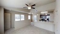 This two-story residence offers a thoughtfully designed open-concept layout that seamlessly connects the living area and kitchen, creating a spacious and functional environment. The main living space features plush carpeting, a ceiling fan with integrated lighting, and a tray ceiling detail that adds architectural interest and a sense of height. Multiple windows along the exterior walls flood the room with natural light, contributing to a bright and welcoming ambiance.

The kitchen is positioned adjacent to the living area and is equipped with dark espresso-toned cabinetry, stainless steel appliances including a gas range and microwave, and light-colored countertops that provide a clean contrast. A peninsula with a built-in sink and pendant lighting overhead serves as both a practical workspace and a natural divider between the kitchen and living areas. A HVAC vent is visible, ensuring climate comfort throughout. The neutral color palette of warm beige tones on both the walls and flooring creates a cohesive and versatile backdrop, making the space easy to personalize. The overall design balances practicality with modern aesthetic appeal across both levels of the home.