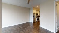 This single-floor unit combines contemporary design with functional living across a well-organized layout. Dark hardwood flooring runs throughout, providing a warm contrast to the neutral beige and white walls that define the space's clean aesthetic. A ceiling fan is centrally positioned in the main living area, enhancing both comfort and airflow.

The living area is highlighted by expansive floor-to-ceiling windows that frame striking urban skyline views, flooding the space with natural light. The open layout transitions seamlessly into the kitchen, which is outfitted with a full suite of stainless steel appliances, including a refrigerator, range, microwave, and dishwasher. White cabinetry extends to the ceiling, complemented by dark granite countertops, a stainless steel undermount sink, and glass-front upper cabinet accents, delivering a polished, modern look.

The bathroom is thoughtfully designed with a backlit LED vanity mirror, granite countertop with an undermount sink, white cabinetry, and a glass-enclosed walk-in shower with white tile surround. The 3D model indicates the inclusion of in-unit laundry, adding further convenience. Overall, the unit offers a cohesive, modern aesthetic with upscale finishes throughout.