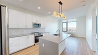 Located at 8601 Bergenline Avenue in North Bergen, NJ, this thoughtfully designed one-bedroom, one-bathroom residence offers a clean, modern aesthetic across a well-utilized single floor. The open-concept kitchen and living area serves as the heart of the home, anchored by a large central island topped with elegant stone countertops and fitted with an undermount sink. The kitchen features crisp white shaker cabinetry, a classic tile backsplash, stainless steel appliances, and a striking multi-globe pendant light that adds a contemporary focal point. Light hardwood flooring flows seamlessly throughout the entire space, enhancing its bright and airy character. The bedroom is generously proportioned and benefits from expansive floor-to-ceiling windows that frame sweeping elevated views of the surrounding North Bergen skyline and beyond, flooding the room with abundant natural light. The bathroom is a standout feature, showcasing large-format marble-look tile from floor to ceiling in the walk-in shower, complemented by brushed gold fixtures that add a luxurious touch. Additional conveniences include two closets and an in-unit laundry area, making this a highly functional and stylish residence.