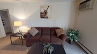 This single-floor unit offers a practical and comfortable layout across several well-defined living spaces. The living room serves as the central gathering area, featuring wall-to-wall carpeting, a wall-mounted air conditioning unit, and a large sliding glass door with vertical blinds that allows natural light to fill the room. A baseboard heating system provides additional climate control throughout.

The galley-style kitchen is efficiently designed with white cabinetry lining both walls, offering ample storage space. It is equipped with a gas range, a full-size refrigerator, a dishwasher, and a stainless steel sink. Light-colored tile flooring and overhead fluorescent lighting keep the space bright and functional. The kitchen opens directly into an adjacent room, enhancing the flow between areas.

The bedroom is a quiet, carpeted retreat featuring a built-in double closet with sliding doors for generous storage. A window with vertical blinds admits natural light, while a baseboard heater ensures year-round comfort.

The bathroom is clean and well-appointed, with white tile walls surrounding a full bathtub and shower combination, mosaic tile flooring, a white vanity, and a toilet. The layout is straightforward and functional.

Overall, this unit presents a neutral, move-in-ready interior with consistent finishes throughout, offering a practical and livable space.