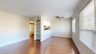 This single-floor unit showcases a consistent design language anchored by painted white brick walls that carry throughout the main living areas, lending a distinct character to the interior. The living room is a welcoming, open space featuring warm wood-look flooring, a ceiling fan, and a built-in shelving unit that adds functional storage and visual interest. A pass-through opening connects the living area to the kitchen, which is equipped with white cabinetry, a refrigerator, and a range, finished with a tile backsplash accent. Natural light enters freely through multiple windows fitted with horizontal blinds, brightening the living spaces throughout the day. The entry area transitions from tile flooring at the front door to the wood-look floors of the main living space, offering a clean and practical welcome zone. The bedroom is carpeted for comfort and features painted brick wall accents, dual windows that allow generous natural light, and a dedicated closet with a rod for ample storage. The bathroom includes a full tub-and-shower combination with white tile surround and a window for added ventilation. Textured ceilings are present throughout the unit, contributing to the overall classic character of this well-laid-out space.