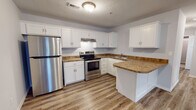 Located at 124 Hamlet Rd in Branson, Missouri, this single-floor unit offers a clean, modern layout designed for comfortable everyday living. The kitchen serves as a functional centerpiece, outfitted with white shaker-style cabinetry, granite-look countertops, and a full suite of stainless steel appliances including a refrigerator and electric range. A peninsula provides additional counter space and creates a natural transition between the kitchen and the adjacent living area. Light wood-tone vinyl plank flooring runs throughout the kitchen and common areas, lending warmth and easy maintenance to the space. The living area features soft neutral walls and light-toned flooring, creating a bright, open feel. The bedrooms are carpeted for comfort and each includes a ceiling fan with light fixture. Windows fitted with blinds allow natural light to filter in while maintaining privacy. The bathroom is finished with consistent design details, including matching white cabinetry, granite-look countertops, a single-sink vanity, and light wood-tone vinyl plank flooring that ties the space together cohesively. Throughout the unit, a neutral color palette of soft grays and whites creates a clean, contemporary atmosphere that is both versatile and inviting.