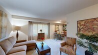 This thoughtfully designed one-bedroom, one-bathroom residence offers an efficient and comfortable layout across a single floor. The open living and dining area serves as the heart of the home, featuring neutral-toned carpet, soft recessed lighting, and large windows dressed with horizontal blinds and draping curtains that invite generous natural light. The living space accommodates both a relaxed seating arrangement and a dedicated dining nook, making it ideal for everyday living and entertaining alike.

The galley-style kitchen is equipped with warm oak cabinetry, white countertops, a stainless steel sink, a dishwasher, and black appliances including a full-size refrigerator, providing ample storage and functionality in a compact footprint.

The bedroom is a serene retreat, featuring plush carpeting, multiple windows with soft window treatments, a dedicated closet with bifold doors, and enough space to comfortably accommodate a full bedroom suite including a desk area. The full bathroom includes a tub-shower combination, a vanity with oak cabinetry, white countertops, and tile flooring, completing the unit's practical amenities. Throughout, the residence maintains a warm, neutral palette that creates a welcoming and cohesive ambiance.