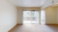 This two-story residence located on Genesee Avenue in San Diego offers a straightforward, functional layout spread across two levels. The living area is a highlight of the main floor, featuring neutral wall-to-wall carpeting and generous natural light delivered through wide sliding glass doors fitted with vertical blinds. The doors open to an outdoor space and frame views of surrounding greenery, creating a bright and airy atmosphere throughout.

The galley-style kitchen is efficiently organized, featuring white cabinetry that extends to the ceiling for ample storage, gray laminate countertops lining both sides, a double-basin sink, and white appliances including an electric range and dishwasher. The kitchen and both bathrooms are finished with warm hardwood-style flooring, providing a practical contrast to the carpeted areas.

Two bathrooms serve the residence. A half bath on one level includes a vanity with a white sink, a lighted mirror, and a privacy window that allows natural light. The full bathroom features a tub-shower combination, a toilet, and a single vanity. The carpeted bedrooms are generously proportioned, with clean white walls and sliding-door closets offering built-in shelving. The overall aesthetic is clean and neutral, well-suited for comfortable everyday living.
