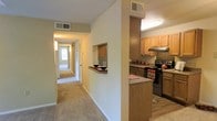This single-floor residence offers a thoughtfully arranged layout that balances functionality and comfort throughout its multiple rooms and living areas. The floor plan reveals a generous central corridor that connects the various spaces, providing a natural flow from one room to the next.

The kitchen is a standout feature, equipped with oak cabinetry, granite-style countertops, a full suite of appliances including an electric range, and a convenient pass-through window that opens to the hallway — ideal for everyday interaction and casual serving. The tiled kitchen floor contrasts nicely with the warm, neutral carpeting found throughout the rest of the home.

A long, well-lit hallway serves as the spine of the residence, leading to multiple rooms that include what appear to be bedrooms and bathrooms. The hallway benefits from natural light filtering in from a window at its far end, creating an open and airy feel. Closets along the corridor provide ample storage.

The layout, as seen in the floor plan, includes a notably spacious living area toward one end of the home, offering room for a variety of furniture arrangements. Overhead ventilation is present throughout, ensuring consistent climate control. The neutral color palette and consistent flooring choices lend the space a cohesive, welcoming ambiance throughout.