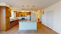 This single-floor residence offers a well-designed layout that balances functionality and comfort throughout its living spaces. The kitchen serves as a central highlight, showcasing warm honey-toned cabinetry, granite countertops, and a full suite of stainless steel appliances, including a gas range, microwave, refrigerator, and dishwasher. A large center island with a matching granite surface provides additional workspace and casual seating potential. Pendant lighting above the island and track lighting add layered illumination, while hardwood-style flooring flows seamlessly through the kitchen and main living area, creating a cohesive, open feel.

The living space benefits from a sliding glass door flanked by a window, allowing natural light to fill the room and offering views to the outdoors. Bedrooms are finished with plush carpet and feature windows with blinds, providing a quiet, comfortable retreat. The bathroom is well-appointed with a dual-sink vanity topped with granite, warm wood cabinetry, a large mirror, tile flooring, and a shower-tub combination. A dedicated in-unit laundry area accommodates a full-size washer and dryer, adding everyday convenience to this thoughtfully arranged space.