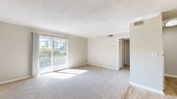 This single-floor unit offers a well-organized layout designed for comfortable everyday living. The spacious living room is a standout feature, finished with plush wall-to-wall carpeting and neutral beige tones that create a calm, inviting atmosphere. Large sliding glass doors flood the space with natural light and open to a private balcony overlooking a landscaped outdoor setting. Crown molding adds a refined finishing touch throughout the main living areas. Adjacent to the living room, the dining area features wood-look flooring, a pendant light fixture, and access to additional rooms, providing a natural transition through the unit. The compact kitchen is efficiently arranged with dark cabinetry, granite-style countertops, a stainless steel sink, and wood-look flooring, along with essential appliances including a refrigerator, stove, and dishwasher. The unit includes two bedrooms, both carpeted and finished in soft neutral tones with textured ceilings and adequate natural light from well-placed windows. The bathroom features a clean, white-tiled tub-shower combination, wood-look flooring, and classic fixtures, maintaining a simple and functional aesthetic throughout.