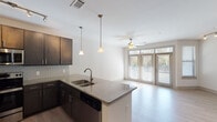 This single-story residence is designed with a clean, modern aesthetic that carries consistently throughout its interior spaces. The open-concept kitchen flows seamlessly into the living area, creating a connected and functional layout ideal for everyday living. The kitchen is outfitted with dark espresso cabinetry, granite countertops, a subway tile backsplash, and stainless steel appliances including a range, microwave, and dishwasher. A peninsula with an undermount double sink and pendant lighting above serves as a natural divider between the kitchen and living space.

The living area features light wood-look flooring, a ceiling fan with light fixture, and large windows with access to an exterior door, allowing abundant natural light and outdoor views. A dedicated bedroom offers plush carpeting, a ceiling fan, and direct access to a bathroom. The bathroom is finished with tile flooring, a dark vanity with granite countertop, a framed mirror, and a lighted vanity bar. A dedicated laundry area accommodates a stacked washer and dryer unit with wire shelving for added storage. Throughout the space, neutral tones and consistent finishes contribute to a cohesive and contemporary atmosphere.