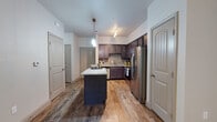 This single-floor residence offers a thoughtfully designed layout that balances functionality and style throughout. The kitchen serves as the centerpiece of the home, showcasing rich dark cabinetry, light granite countertops, and a full suite of stainless steel appliances including a refrigerator with ice maker, range, microwave, and dishwasher. A gray subway tile backsplash adds a modern touch, while a central island with a matching granite surface provides additional prep space and casual seating. Warm wood-look flooring runs throughout the main living areas, complementing the neutral wall tones and creating a cohesive, inviting atmosphere. The living area is generously sized and benefits from natural light through large windows dressed with horizontal blinds, along with a ceiling fan for added comfort. A glass door opens to a private outdoor area, further enhancing the sense of openness. The bedrooms feature plush carpeting and ceiling fans, with one bedroom offering a direct view into an en-suite bathroom. The bathroom is finished with a dark vanity, granite countertop, undermount sink, and a large mirror, maintaining the refined aesthetic found throughout the home. Arched interior doors and clean architectural lines tie the entire space together with consistent, polished detail.