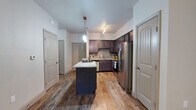 This single-floor residence offers a thoughtfully designed layout that balances functionality and style throughout. The kitchen serves as the centerpiece of the home, showcasing rich dark cabinetry, light granite countertops, and a full suite of stainless steel appliances including a refrigerator with ice maker, range, microwave, and dishwasher. A gray subway tile backsplash adds a modern touch, while a central island with a matching granite surface provides additional prep space and casual seating. Warm wood-look flooring runs throughout the main living areas, complementing the neutral wall tones and creating a cohesive, inviting atmosphere. The living area is generously sized and benefits from natural light through large windows dressed with horizontal blinds, along with a ceiling fan for added comfort. A glass door opens to a private outdoor area, further enhancing the sense of openness. The bedrooms feature plush carpeting and ceiling fans, with one bedroom offering a direct view into an en-suite bathroom. The bathroom is finished with a dark vanity, granite countertop, undermount sink, and a large mirror, maintaining the refined aesthetic found throughout the home. Arched interior doors and clean architectural lines tie the entire space together with consistent, polished detail.