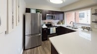 Located at 2424 N Tustin Ave in Santa Ana, California, this two-story residence offers a thoughtfully designed layout with contemporary finishes throughout. The kitchen serves as a functional centerpiece, featuring dark espresso cabinetry, light quartz countertops, stainless steel appliances including a refrigerator, range, and built-in microwave, along with a subway tile backsplash and a double-basin sink positioned beneath a window. Wood-look flooring grounds the space with a warm, clean aesthetic.

The living area is carpeted and comfortably scaled, with neutral-toned walls that create a relaxed atmosphere. A wall-mounted air conditioning unit provides climate control, and windows allow natural light to filter in. The adjacent dining area features wood-look flooring, a ceiling fan with integrated lighting, and sliding door access that brings in additional light.

The bedrooms are carpeted and serene, each offering closet storage. The primary bedroom includes a spacious layout with room for a full suite of furniture. A secondary bedroom also features a built-in closet. The upper level is accessible via a carpeted staircase with white railing. The bathroom includes dark vanity cabinetry, light countertops, wood-look tile flooring, and a mirror, maintaining the cohesive modern palette found throughout the home.