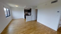 This single-floor space features an open-concept layout that seamlessly connects the living area to the kitchen, creating a cohesive and functional environment. Light hardwood flooring extends throughout, adding warmth and continuity to the space.

The kitchen is well-appointed with dark cabinetry that provides a striking contrast against the white walls and light flooring. Stainless steel appliances, including a range and an over-the-range microwave, are integrated into the design for a modern, polished look. A peninsula-style counter defines the kitchen boundary while maintaining the open flow of the living area.

Recessed lighting in the kitchen ensures functional illumination, complementing the flush ceiling light in the main living area. The white walls and clean lines throughout contribute to a bright and airy atmosphere. The space also includes a door leading to an additional room, providing further utility. Wide baseboards and a neutral palette enhance the overall sense of order and simplicity, making this a versatile space well-suited for a variety of living arrangements.