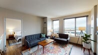 This thoughtfully designed single-floor unit offers a cohesive blend of modern finishes and comfortable living spaces spread across a functional open layout. The living room serves as the heart of the unit, featuring hardwood-style flooring, large windows that frame expansive city skyline views, and ample space for multiple seating arrangements. The area is bright and welcoming, with natural light pouring in from multiple windows that overlook the urban landscape below.

The kitchen is outfitted with warm maple cabinetry, dark granite countertops, stainless steel appliances including a refrigerator, range, and built-in microwave, and light tile flooring — providing a clean, functional workspace for cooking and entertaining.

Two well-sized bedrooms offer restful retreats, each with hardwood-style floors, neutral wall tones, and windows with city views. The bedrooms are calm and understated, with sufficient space for full bedroom furniture arrangements.

Two bathrooms mirror the kitchen's aesthetic, featuring maple vanity cabinetry, dark granite countertops with stainless steel sinks, large mirrors, and tile flooring. One bathroom includes a shower-tub combination, while the other offers a similarly clean, efficient layout.

Overall, the unit presents a consistent, contemporary aesthetic throughout, with urban views as a defining feature.