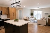 Unit H at 315 Faribault is a thoughtfully designed single-floor residence spanning 1,190 square feet, featuring 5 bedrooms, 2 full bathrooms, and a dedicated laundry room. The open-concept kitchen and living area serves as the heart of the unit, showcasing a large central island with a white quartz countertop, two-tone cabinetry in light wood and charcoal gray, white subway tile backsplash, stainless steel appliances, and a modern industrial pendant light fixture. Recessed lighting and hardwood-style flooring extend throughout, creating a bright, cohesive aesthetic. The living room opens to a private balcony via a sliding glass door, allowing natural light to fill the space. Each of the five bedrooms features the same warm hardwood-style flooring, neutral paint tones, and individual closets with built-in shelving. The primary bedroom measures 130 square feet. Both bathrooms are finished with tile flooring, a tub/shower combo, wood-toned vanity, white countertop, round mirror, and industrial-style light fixtures. The in-unit laundry room houses a full-size Maytag washer and dryer with an overhead storage shelf, adding everyday convenience to this well-appointed rental unit.