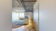 Located at 2360 Lawrence St in Denver, CO, this single-floor unit offers an industrial-modern aesthetic defined by its striking exposed concrete ceiling with visible pipe runs and track lighting throughout the main living area. The open layout connects the kitchen and living space efficiently, creating a cohesive common area despite the compact overall footprint.

The kitchen is outfitted with light maple cabinetry, dark countertops, a black electric range, a full-size refrigerator, and a peninsula with a double sink that separates the kitchen from the carpeted living area. Checkered vinyl tile flooring runs through the kitchen and bathroom, providing a retro contrast to the industrial ceiling above.

The four bedrooms are carpeted and vary in size, with the primary bedroom featuring corner windows on two walls that allow abundant natural light and panoramic views of the surrounding Denver cityscape. Additional bedrooms include closets and share the exposed concrete ceiling aesthetic. The single full bathroom includes a vanity with dark countertop, a tub-shower combo, and matching checkered tile flooring. Each room benefits from the elevated position of the unit, offering open sky and city views.