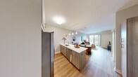 This thoughtfully designed one-bedroom, one-bathroom residence at 1100 Broadway Street in Ann Arbor, Michigan offers a contemporary living experience with a well-organized, open-concept floor plan. Light oak-toned hardwood flooring runs throughout, creating a cohesive and modern aesthetic.

The kitchen and living area flow seamlessly together, centered around a sleek peninsula with a white quartz countertop, an undermount sink, and bar seating for casual dining. The kitchen is equipped with stainless steel appliances—including a French door refrigerator, gas range, and built-in microwave—complemented by a mix of white upper cabinets and warm wood-toned lower cabinetry. Pendant lighting above the peninsula adds a refined touch.

The living room is bright and airy, with a sliding glass door that opens to a private balcony overlooking outdoor greenery. Track lighting provides flexible illumination throughout.

The bedroom is a comfortable retreat, featuring a large window that fills the room with natural light and offers views of the surrounding area. A dedicated closet provides convenient storage.

The bathroom features a clean, modern design with a white vanity, ample cabinetry, a large mirror, and hardwood-style flooring. The unit also includes additional storage accessible from the kitchen area.
