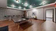 Located at 608 Second Ave S in downtown Minneapolis, this generously sized amenity space spans a single floor and is thoughtfully divided into distinct entertainment zones, offering a diverse range of social and leisure activities.

The main game room is an eye-catching centerpiece, featuring a bold teal tray ceiling with recessed lighting that creates a vibrant, energetic atmosphere. A retro-patterned accent wall adds a playful, mid-century modern flair, while warm hardwood flooring grounds the space. A full-size ping-pong table takes center stage, accompanied by a wet bar with a sink, perfect for hosting gatherings. Framed black-and-white photography adds a curated, gallery-like touch to the walls.

An adjacent carpeted zone expands the entertainment options further, housing classic arcade cabinets — including a Pong machine — a shuffleboard table, and a foosball table. High-top bar seating with framed artwork creates a casual social corner, while recessed lighting keeps the area bright and inviting.

A dedicated media lounge offers a more intimate retreat, furnished with a tufted caramel leather sectional sofa, a wooden credenza, and a large wall-mounted display screen — ideal for movie nights or casual viewing. A smaller, cozy nook adjacent to the lounge provides a quiet seating area for more private conversations.

Together, these spaces form a well-rounded, amenity-rich environment designed for both lively entertainment and relaxed socializing.