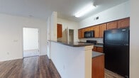 This single-floor residence is thoughtfully designed to maximize functionality and comfort. The open-concept living area is anchored by rich, dark hardwood-style flooring that extends throughout the main living spaces, creating a warm and cohesive aesthetic. Large windows and a glass door in the living room flood the space with natural light, while a ceiling fan adds practicality. The layout flows seamlessly from the living area toward the kitchen, which is separated by a peninsula-style breakfast bar with dark countertops, offering both additional workspace and a casual dining option.

The kitchen is well-appointed with warm-toned wood cabinetry, dark granite-style countertops, and a full suite of black appliances, including a refrigerator, electric range, and over-the-range microwave. A dedicated pantry closet provides ample storage, and the double-basin sink completes the functional layout.

The bedrooms are carpeted and feature neutral walls, ceiling fans, and blinds-covered windows that allow for natural light. Each room offers a comfortable and quiet retreat. The bathrooms are clean and straightforward, each featuring a soaking tub and shower combination with white surrounds and chrome fixtures, maintaining a consistent, simple aesthetic throughout the residence.