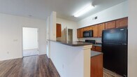 This single-floor residence is thoughtfully designed to maximize functionality and comfort. The open-concept living area is anchored by rich, dark hardwood-style flooring that extends throughout the main living spaces, creating a warm and cohesive aesthetic. Large windows and a glass door in the living room flood the space with natural light, while a ceiling fan adds practicality. The layout flows seamlessly from the living area toward the kitchen, which is separated by a peninsula-style breakfast bar with dark countertops, offering both additional workspace and a casual dining option.

The kitchen is well-appointed with warm-toned wood cabinetry, dark granite-style countertops, and a full suite of black appliances, including a refrigerator, electric range, and over-the-range microwave. A dedicated pantry closet provides ample storage, and the double-basin sink completes the functional layout.

The bedrooms are carpeted and feature neutral walls, ceiling fans, and blinds-covered windows that allow for natural light. Each room offers a comfortable and quiet retreat. The bathrooms are clean and straightforward, each featuring a soaking tub and shower combination with white surrounds and chrome fixtures, maintaining a consistent, simple aesthetic throughout the residence.