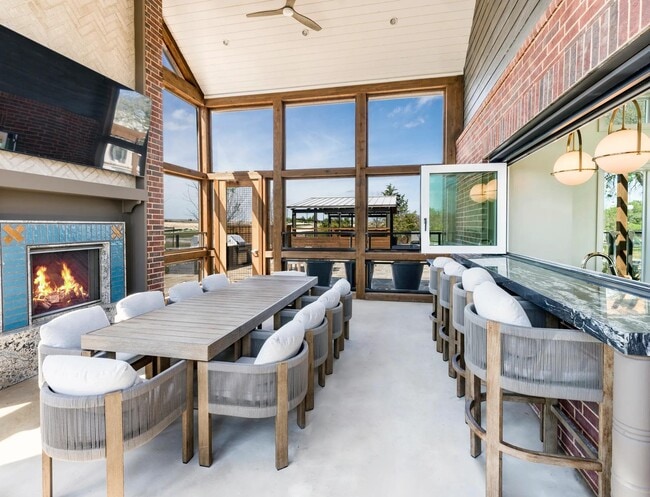 Screened-in porch with a harvest dining table, an adjacent catering kitchen and entertainment lounge inside, plus a cozy outdoor fireplace. - Modera McKinney Ridge