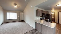 This two-floor home offers a well-organized layout designed for comfortable everyday living. The main level opens into a living area characterized by soaring vaulted ceilings and a combination of wood-look flooring and plush carpeting. A ceiling fan adds practicality to the living space, which flows naturally toward the front entry. The kitchen is thoughtfully designed with dark cabinetry, light countertops, and black appliances including a refrigerator, range, and microwave. A double stainless steel sink sits beneath a window, and a peninsula counter provides additional workspace. A staircase with carpeted treads leads to the upper floor, where multiple bedrooms await. Each bedroom features soft carpeting, neutral-toned walls, and windows that allow natural light to fill the rooms. Vaulted ceiling lines carry into some of the upper-level spaces, adding architectural interest. A full bathroom on the upper level is finished with tile flooring, a dark-stained vanity with a single sink, and a tub-shower combination with clean white surround. The neutral color palette and consistent finishes throughout create a cohesive and move-in-ready atmosphere across both floors.
