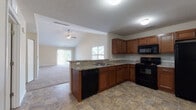 Located at 1802 Kelly's Path in Reynoldsburg, Ohio, this single-story home offers a well-designed, open layout that maximizes both functionality and comfort. The kitchen is a central highlight, featuring warm medium-toned cabinetry, granite-look countertops, and a full suite of black appliances including a range, over-the-range microwave, dishwasher, and refrigerator. Stone-look tile flooring runs throughout the kitchen and extends into the adjacent areas, providing a durable and cohesive aesthetic. A peninsula with a sink connects the kitchen to the spacious living area, which boasts vaulted ceilings with a ceiling fan and an abundance of natural light from large windows and a sliding glass door. The living area is finished with plush wall-to-wall carpeting. The bedrooms are generously sized, each featuring carpet flooring and windows that bring in natural light. The bathrooms are finished with matching tile flooring and rich wood-toned vanities; one bathroom includes a soaking tub, while another features a walk-in shower. The attached two-car garage provides ample storage and parking space, complete with an automatic opener. Textured ceilings are found throughout the home, adding a consistent finishing detail across the single-floor layout.
