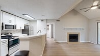 This 2-bedroom, 1-bathroom residence in Raleigh, NC offers a well-designed single-floor layout with a bright, neutral palette and light wood-style flooring throughout. The living room is a standout, featuring dramatic vaulted ceilings, a ceiling fan, a tile-surround wood-burning fireplace with a floating mantel shelf, and a sliding glass door that opens to an outdoor balcony with lush tree views. The open kitchen includes white cabinetry, a tile backsplash, stainless steel appliances, and a curved peninsula with a black matte faucet that connects seamlessly to the living area. Both bedrooms receive generous natural light through large windows with serene wooded views. The primary bedroom includes built-in open shelving with warm wood tones, an integrated desk with white cabinetry, and a walk-in closet. The second bedroom is spacious and airy with a large corner window. A dedicated walk-in closet with multi-level shelving and hanging rods provides excellent storage. The bathroom features a tub-shower combo, wood-style flooring, and matte black hardware accents. A hallway connects all rooms efficiently, completing this well-appointed Raleigh residence.