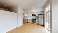 This contemporary single-floor unit offers a clean, modern aesthetic defined by crisp white walls, light wood flooring, and an open-concept layout that maximizes the sense of space. The kitchen is well-appointed with full-height white upper cabinetry, warm wood-toned lower cabinets, a tile backsplash, and a complete suite of stainless steel appliances including a gas range, built-in microwave, dishwasher, and refrigerator. A deep utility sink and recessed lighting complete the functional yet stylish kitchen space. Large floor-to-ceiling windows and additional oversized windows in the living area flood the interior with natural light and provide views of the surrounding neighborhood. The open living space is generous and versatile, with clean lines and neutral tones that offer a blank canvas for any layout. A dedicated hallway connects the main living areas to the private spaces, flanked by full-height built-in storage cabinetry offering ample organizational capacity, as well as a closet with built-in shelving. The bathroom features a wood-toned vanity with a white countertop, a large mirror, and distinctive hexagonal tile flooring in soft gray tones, creating a calm and modern atmosphere. Throughout the unit, recessed lighting, clean baseboards, and consistent finishes reinforce a cohesive, well-designed interior.