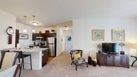 Located at 457 Dutch Meadows Ln in Schenectady, NY, this single-floor residence offers a well-designed, open-concept layout that seamlessly connects the kitchen, dining, and living areas. The kitchen is appointed with dark espresso cabinetry, stainless steel appliances including a refrigerator, microwave, and range, and a granite-topped island with pendant lighting overhead. Hardwood-style flooring anchors the kitchen and dining area, while plush carpeting extends through the living room and hallways, creating a warm and comfortable atmosphere. The living room is generously proportioned, featuring neutral walls that allow for flexible styling and access to natural light through large windows. A dedicated dining space sits adjacent to the main living area, providing a functional and inviting setting for meals. The two bedrooms are bright and well-sized, each benefiting from large windows that bring in abundant natural light and outdoor views. The primary bedroom is notably spacious with direct exterior access. Two bathrooms serve the residence, each finished with tile flooring, a tub-shower combination, and clean white vanities with ample storage. Built-in shelving in the bathroom adds practical organizational space. The overall design is clean, modern, and move-in ready.