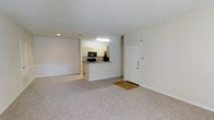 This single-floor residence offers a clean, open layout designed for comfortable everyday living. The main living area is spacious and filled with natural light, featuring neutral-toned carpeting that extends throughout, white walls, and a smooth ceiling with recessed lighting that creates a bright, welcoming ambiance.

The kitchen is positioned at the heart of the home and is well-equipped with cream-colored cabinetry, dark stone-look countertops, and black appliances including a microwave and refrigerator. A peninsula-style breakfast bar separates the kitchen from the living area, providing both additional counter space and a casual dining option, while maintaining the open flow between rooms.

The front entryway features a classic paneled white door with a small foyer area, transitioning seamlessly into the main living space. The overall color palette is consistent and understated, with white trim, neutral walls, and light carpeting working together to create a cohesive and versatile interior. The layout is efficient and practical, making excellent use of the available footprint. The space is move-in ready and well-suited for a variety of furniture arrangements and personal styles.
