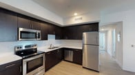 This single-floor unit showcases a cohesive modern design throughout its well-organized layout. The kitchen serves as a standout feature, equipped with dark espresso-finish cabinetry that extends floor to ceiling, providing ample storage. Crisp white countertops offer generous workspace and contrast sharply against the dark cabinetry. A full suite of stainless steel appliances includes an electric range, built-in microwave, dishwasher, and refrigerator. Light wood-tone flooring runs throughout the kitchen, adding warmth to the contemporary aesthetic.

The bathroom maintains a clean, minimalist design with white tile surrounding a full soaking tub and shower combination. Brushed nickel fixtures complement the light wood-tone flooring carried over from the main living areas, and a small window allows natural light to brighten the space.

The bedroom features neutral carpet flooring, crisp white walls, and a window fitted with horizontal blinds, allowing for adjustable natural light. The 3D floor plan reveals a thoughtfully arranged layout connecting the kitchen, living area, bedroom, and bathroom in a functional and efficient configuration throughout the single floor.
