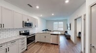 This well-appointed 1-bedroom, 1-bathroom unit offers a thoughtfully designed layout that maximizes functionality and comfort. The open-concept kitchen and living area serves as the heart of the space, where a fully equipped kitchen features gray shaker-style cabinetry, granite countertops, a white subway tile backsplash, and a full suite of stainless steel appliances including a refrigerator, electric range, microwave, and dishwasher. A peninsula with an integrated sink provides additional prep space and doubles as a casual dining area. The living area flows seamlessly from the kitchen, offering a bright, welcoming space with natural light streaming through large windows fitted with blinds. Warm wood-look flooring extends throughout the entire unit, creating a cohesive and modern aesthetic. The bedroom is a comfortable, well-lit room with a ceiling fan, a window with outdoor views, and ample space for furnishings. A dedicated closet provides convenient storage. The bathroom is clean and modern, featuring a granite-topped vanity with shaker cabinetry, a tub-shower combination with white subway tile surround, and wood-look flooring. A louvered closet door near the entry adds a classic touch to the otherwise contemporary design.