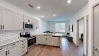 This well-appointed 1-bedroom, 1-bathroom unit offers a thoughtfully designed layout that maximizes functionality and comfort. The open-concept kitchen and living area serves as the heart of the space, where a fully equipped kitchen features gray shaker-style cabinetry, granite countertops, a white subway tile backsplash, and a full suite of stainless steel appliances including a refrigerator, electric range, microwave, and dishwasher. A peninsula with an integrated sink provides additional prep space and doubles as a casual dining area. The living area flows seamlessly from the kitchen, offering a bright, welcoming space with natural light streaming through large windows fitted with blinds. Warm wood-look flooring extends throughout the entire unit, creating a cohesive and modern aesthetic. The bedroom is a comfortable, well-lit room with a ceiling fan, a window with outdoor views, and ample space for furnishings. A dedicated closet provides convenient storage. The bathroom is clean and modern, featuring a granite-topped vanity with shaker cabinetry, a tub-shower combination with white subway tile surround, and wood-look flooring. A louvered closet door near the entry adds a classic touch to the otherwise contemporary design.