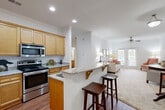 This well-appointed 2-bedroom, 2-bathroom residence in Greensboro, NC offers a thoughtfully designed single-floor layout that maximizes both comfort and functionality. The open-concept kitchen flows seamlessly into the living area, anchored by a granite-topped breakfast bar with seating — ideal for casual dining or entertaining. The kitchen is outfitted with warm honey-toned cabinetry, stainless steel appliances including a dishwasher, microwave, and refrigerator, complemented by hardwood-style flooring and recessed lighting. Crown molding adds a refined touch throughout the main living areas. The bright living room features plush carpeting, a ceiling fan, and French doors that invite natural light while opening to an outdoor balcony. Both bedrooms are carpeted and include ceiling fans, with the primary bedroom offering a spacious walk-in closet with wire shelving. Each bathroom is finished with granite-accented vanities and hardwood-style flooring, with one bathroom featuring a full tub-shower combination. Additional closet storage is also provided. The overall ambiance is clean, light-filled, and move-in ready, reflecting a comfortable and practical living environment.