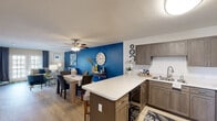 Located at 4636 Canterbury Dr in Myrtle Beach, SC, this single-floor home offers a cohesive coastal-inspired design throughout. The open-concept layout connects the kitchen, dining, and living areas into one seamless, functional space. The kitchen features rich taupe cabinetry, quartz countertops, a center island with bar seating, and black appliances including a refrigerator, range, and microwave. Hardwood-style flooring extends across the main living areas, adding warmth and continuity.

The living room is anchored by a bold blue accent wall, large sliding glass door that invites natural light, and a built-in wood media wall with shelving. The adjacent dining area maintains the vibrant blue accent, creating a lively and cohesive atmosphere. Ceiling fans throughout ensure year-round comfort.

The primary bedroom features a soothing blue accent wall, plush carpeting, and a ceiling fan, providing a relaxing retreat. A second bedroom, also with a navy accent wall and ceiling fan, comfortably accommodates twin beds.

Two full bathrooms serve the home, each featuring wood-toned vanities, quartz countertops, and tub-shower combinations. The overall design reflects a consistent nautical color palette of navy, teal, and white, giving the entire home a polished, beach-inspired character.