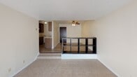 This single-floor residential unit offers a practical and comfortable layout across several well-defined living spaces. The living area is carpeted and bathed in natural light through a large sliding glass door fitted with vertical blinds, which also provides outdoor views. A wall-mounted air conditioning unit and baseboard heating ensure year-round climate control. A low open-shelf divider visually separates the living area from the adjacent dining or entryway space, where wood-look flooring begins and a ceiling fan with light fixture overhead adds both function and airflow.

The galley-style kitchen is efficiently designed with dark wood cabinetry, laminate countertops, a stainless steel double sink, and white appliances including a refrigerator, electric coil range, and overhead microwave. Open shelving adds additional storage and display space, while wood-look flooring ties the room together cohesively.

The bedroom is generously sized with soft carpeting, neutral walls, and baseboard heating, creating a quiet and restful retreat. The full bathroom features a dark-toned vanity with a granite-style countertop, a tiled mosaic floor, and a full tub-shower combination with clean white tile surround. The overall aesthetic throughout the unit is clean, neutral, and move-in ready.
