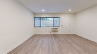 Located on S Normandie Ave in the heart of Los Angeles, this thoughtfully designed one-bedroom, one-bathroom unit offers a clean, modern aesthetic with consistent light wood flooring and crisp white walls throughout. The open-concept living and kitchen area forms the heart of the unit, with recessed lighting overhead and a wide window fitted with vertical blinds that brings in natural light. A wall-mounted HVAC unit provides climate control directly from the main living space. The kitchen is well-appointed with white shaker-style cabinetry, quartz countertops, stainless steel appliances including a gas range and full-size refrigerator, an integrated dishwasher, and a stainless undermount sink — offering both functionality and a polished look. The bedroom features full-length mirrored sliding closet doors that enhance the sense of space, along with direct access to a private balcony with a slatted wood-and-steel railing that overlooks the surrounding neighborhood. The bathroom is finished with a white shaker vanity, quartz countertop, undermount sink, and a full tub-shower combination with white tile surround. The unit presents a cohesive, move-in-ready interior throughout.