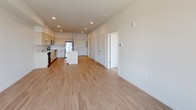 This contemporary single-floor unit showcases a clean, modern design with a thoughtful open-concept layout. The kitchen is well-appointed with light wood cabinetry extending to the ceiling, stainless steel appliances including a refrigerator, range, microwave, and dishwasher, and a sleek white quartz countertop island that doubles as a breakfast bar. Light hardwood-style flooring flows seamlessly through the kitchen and living areas, creating a bright and cohesive aesthetic. Recessed lighting throughout ensures consistent illumination across the space.

The open living area is generously proportioned, offering flexibility for furniture arrangement, and transitions easily from the kitchen. Large windows invite abundant natural light and frame views of the surrounding urban neighborhood.

The carpeted bedroom provides a comfortable retreat, featuring a ceiling fan, a large window with sweeping city views, and direct access to a spacious walk-in closet with built-in shelving. A second room, also accessible from the main living area, offers additional flexible living space.

The full bathroom is finished with a wide vanity topped with white countertops, light wood cabinetry, a large mirror, and a tub-shower combination, all set against a neutral, light-toned floor. The overall design palette — soft whites, light woods, and warm neutrals — gives the entire unit a fresh, contemporary feel.