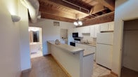 This two-story space showcases a compelling blend of industrial character and functional design. Exposed red brick walls are a defining architectural feature throughout, lending warmth and texture to the interior. The ceilings reveal original heavy timber beams alongside visible ductwork and piping, reinforcing the loft-inspired aesthetic. Natural light filters in through windows on both levels, highlighting the raw beauty of the brick and the open layout.

The kitchen is well-appointed with white cabinetry, a full suite of appliances including a refrigerator, electric range, built-in microwave, and dishwasher, all anchored by a generous peninsula that provides additional prep and seating space. Tile flooring transitions seamlessly from the kitchen into the adjoining areas. A dedicated laundry area houses a full-size washer and dryer, adding everyday convenience.

Two bathrooms serve the space—one on each level. Both are clean and functional, featuring vanities with large mirrors, and one includes a full tub and shower combination. Carpeted living areas on both floors offer a softer contrast to the surrounding industrial elements. A staircase connects the two levels, where the upper floor continues the exposed brick and beam aesthetic, bathed in natural light from multiple windows.
